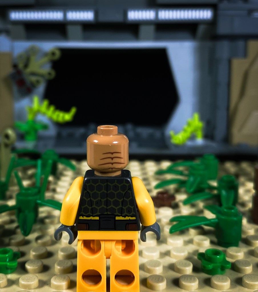 Minifigura de LEGO frente a una base abandonada en medio del bosque, a punto de entrar en ella.