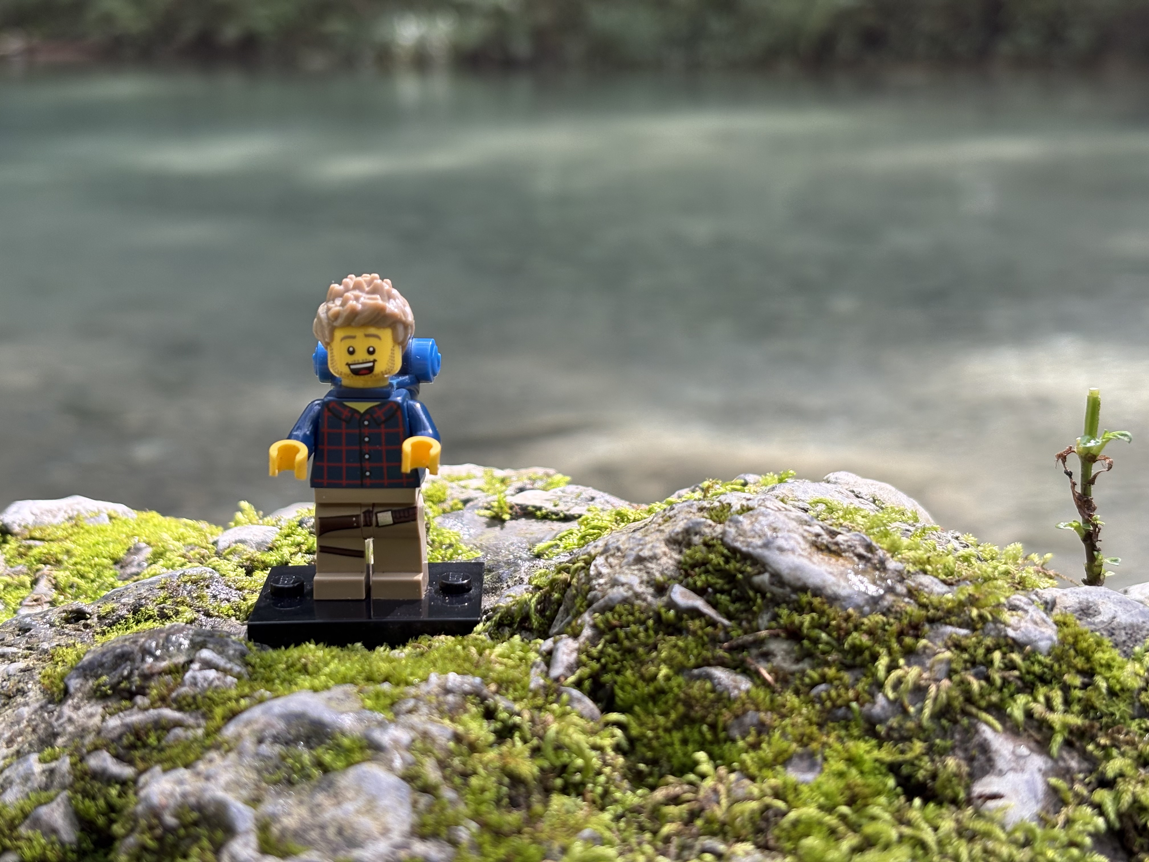 Minifigura de LEGO sonriendo en medio de un bosque, con un río al fondo.