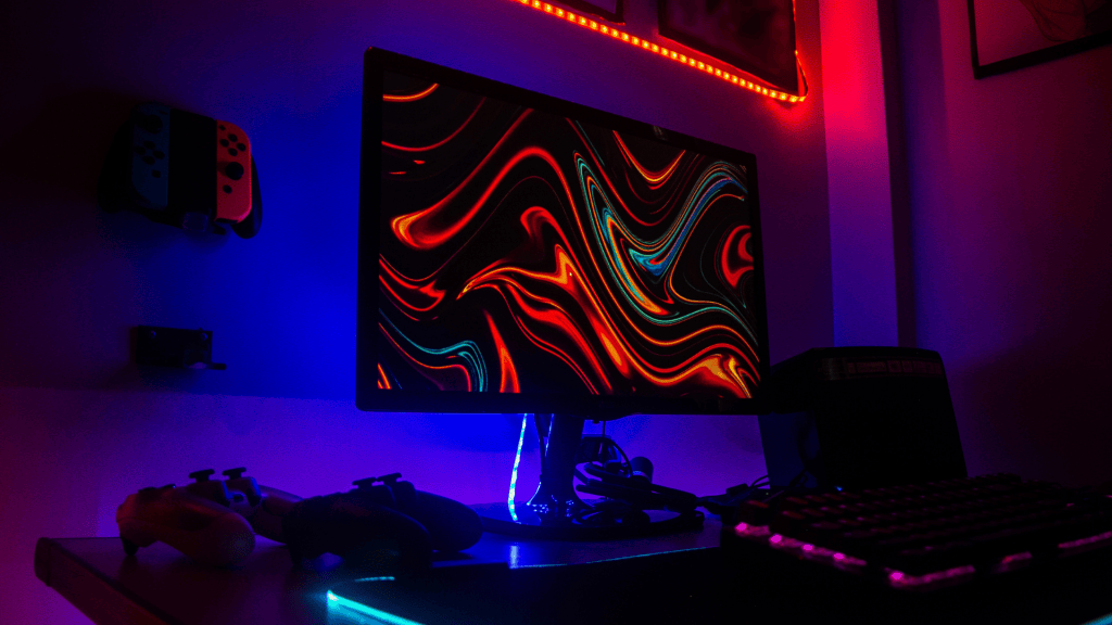 Setup gaming con monitor, teclado y controles iluminados con luces de colores.
